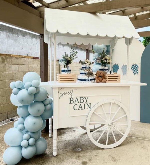 White cart styled with a blue balloon garland and desserts for a baby shower