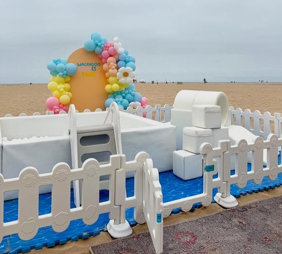 Luxe soft play setup with ball pit, soft climbers, and a pastel balloon arch at a beach party