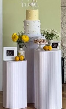 White pedestal display stands with a tiered cake, florals, and lemon accents